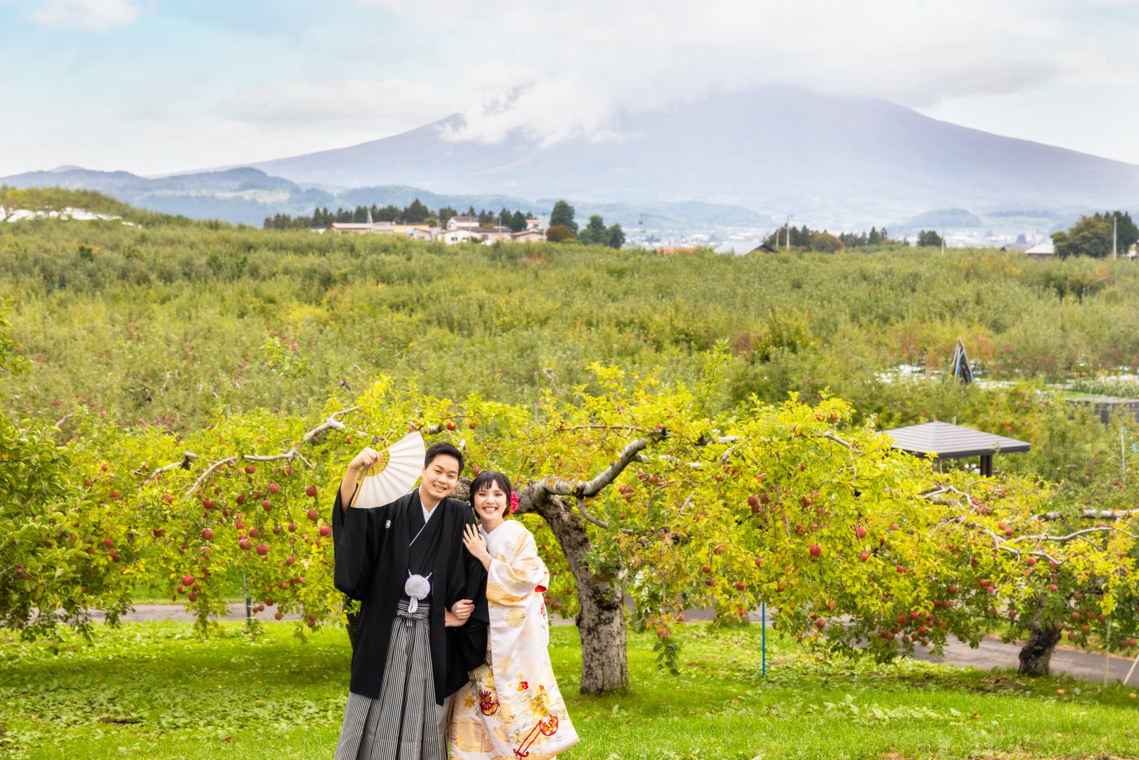 岩木山とりんご畑を背景に並ぶ和装の新郎新婦